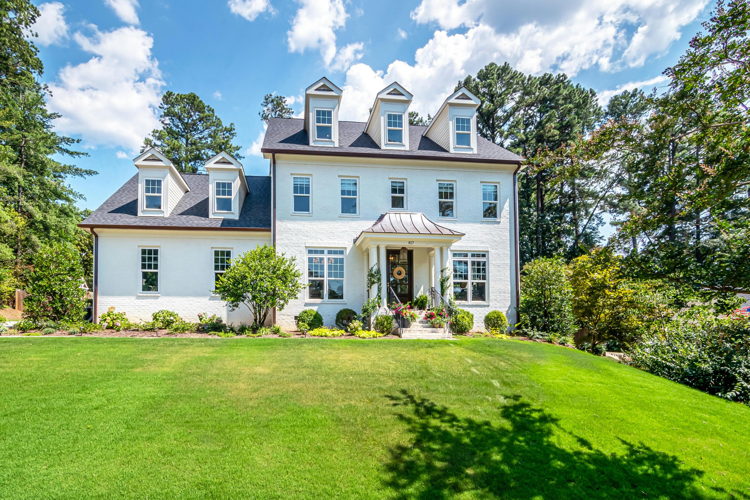 Beautiful colonial-style house with a lush green lawn and blue sky, perfect summer property.